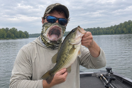 An angler wearing a BassMasks fishing neck gaiter holds a bass beside his matching fish face.